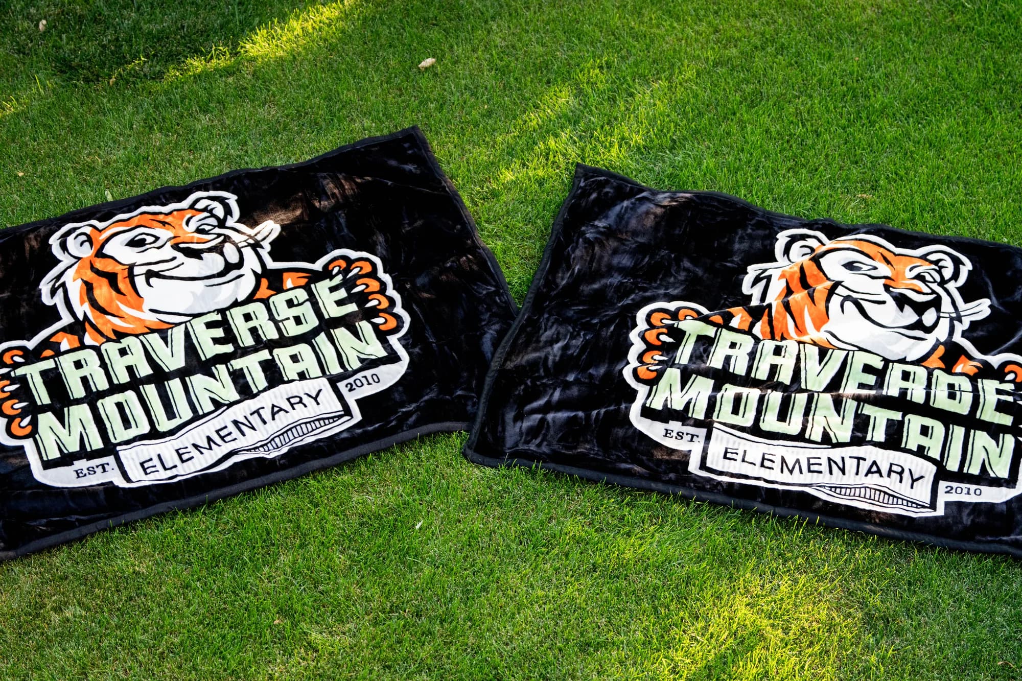 Two Traverse Mountain Elementary tiger mascot blankets laid out side by side, two in-house layouts of the same school identity