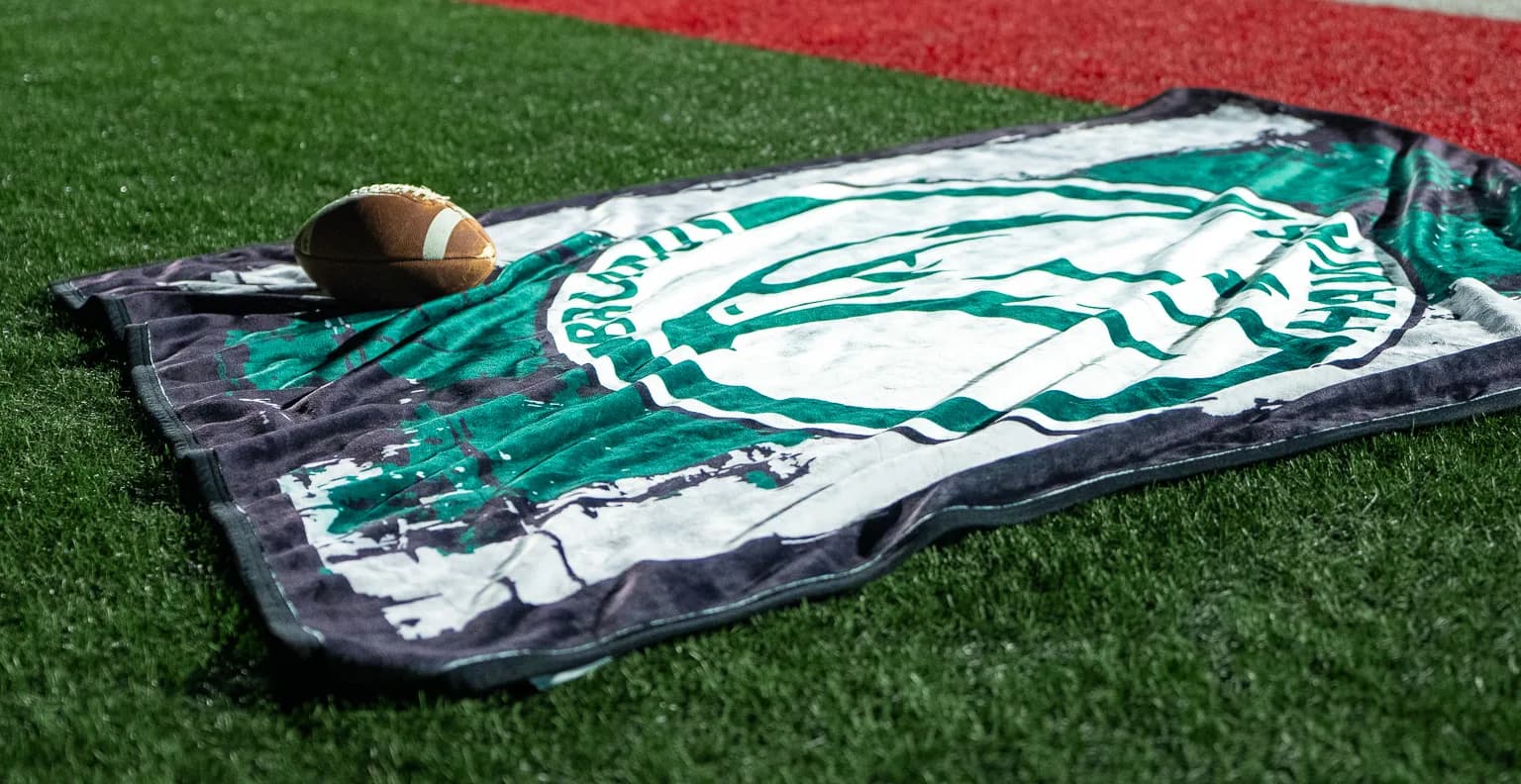 A green Bruins mascot blanket laid out in the endzone under the stadium lights at night